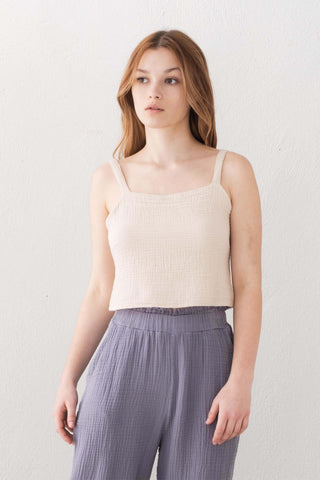 Woman wearing a beige tank top and gray pants against a white background